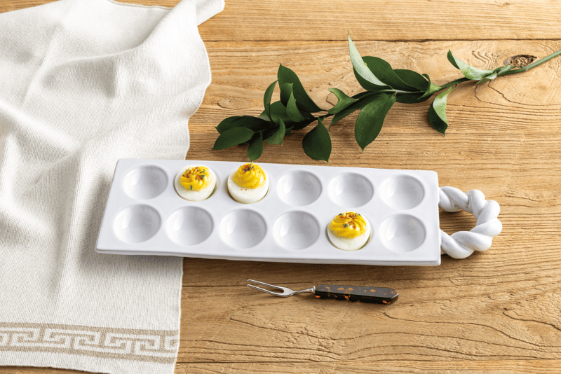 White deviled tray with a handle on a white background with serving fork