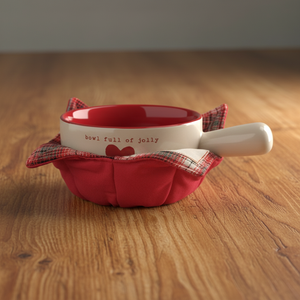 A red and white ceramic bowl with a white handle, nestled inside a red fabric pouch with a plaid trim. The bowl is printed with the phrase 'bowl full of jolly' and a small red heart.
