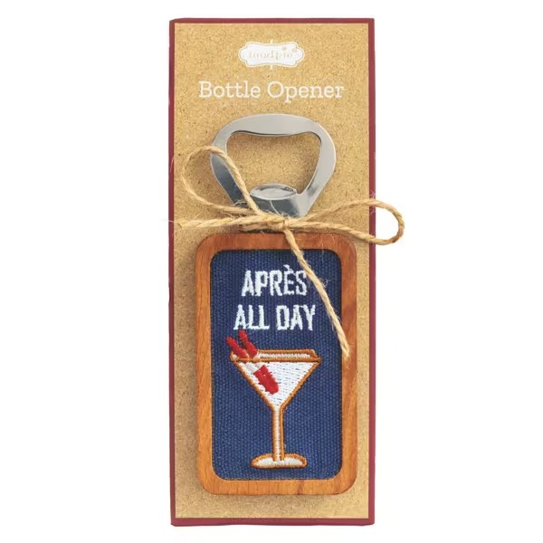 A bottle opener presented on its kraft paper backing card. The opener features a wooden frame with a blue embroidered fabric panel that reads 'APRÈS ALL DAY' above an embroidered martini glass with red garnishes.